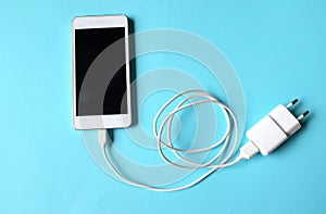 Close up white Smartphone Plug In with Charger Adapter on Blue Background