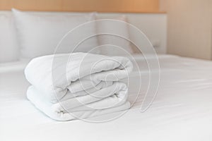 Close-up: The white towels are neatly folded and placed on the white bed. Hotel