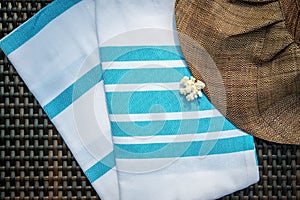 Close-up of white and turquoise color Turkish peshtemal / towel, white seashells and straw hat on rattan lounger.