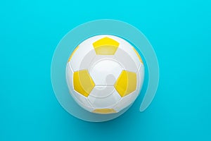 Close-up of white and yellow soccer ball in centre of turquoise blue background