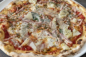 Close-up of a whole pineapple and ham thin crust pizza on a plate abundant in delicious ingredients