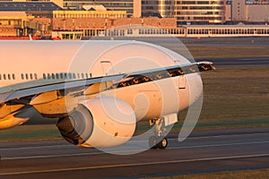 Close up of wide-body passenger aircraft with wing and engine taxing on the runway during sunset. Airplane turns on runway