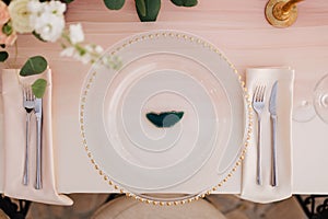 Wedding dinner table reception. Close-up of wildcard with gold beads, transparent glass. Runner of pink silk. Candles in