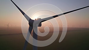 Close-up of wind turbine blades at sunset or sunrise. Windmills with rotating wings among green fields. Technology for wind energy