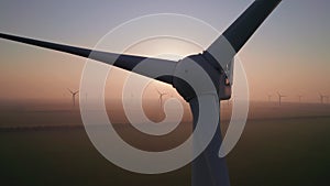 Close-up of wind turbine blades at sunset or sunrise. Windmills with rotating wings among green fields. Technology for wind energy