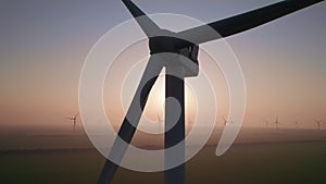 Close-up of wind turbine blades at sunset or sunrise. Windmills with rotating wings among green fields. Technology for wind energy