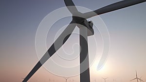 Close-up of wind turbine blades at sunset or sunrise. Windmills with rotating wings among green fields. Technology for wind energy