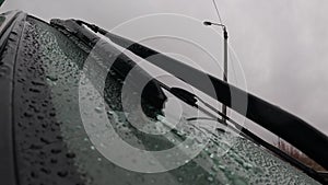 Close-up windshield with rain drops and car wipers passing. Closeup glass on rainy summer day outdoors