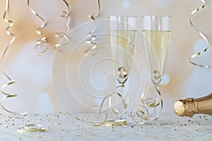 A close up of wine flutes filled with champagne and wedding bands inside the flute, against a bokeh background.