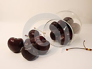 Close up wine glass full of cold dark ripe cherries fell on a table on white background. Healthy lifestyle concept. Ingredients.