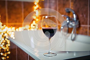 Close up of wine glass with red wine near bathtub with lights on the background, relaxtion and spa concept