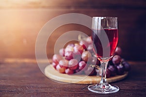 Close-up of a wine glasses  over grape on wood plate against window light  on wooden table