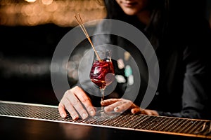 Close-up wineglass with red cocktail which decorated by two sticks stand on bar counter.