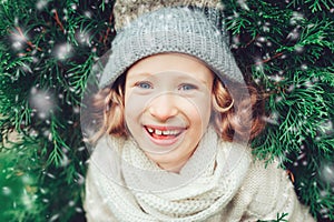 Close up winter portrait of happy child girl wearing warm knitted hat and scarf with Christmas tree