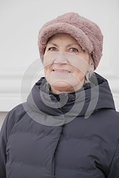Close-up winter portrait of smiling senior woman looking at camera, wearing faux pink fur cap.