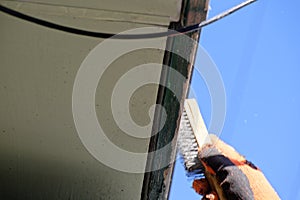 A close up of a wire brush being used to remove loose paint from a bargeboard on a weatherboard house
