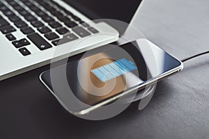 Wireless charging mobile phone on table near to laptop