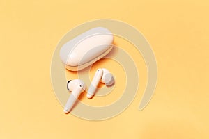 Close-up of wireless earbuds with charger case on pastel yellow background