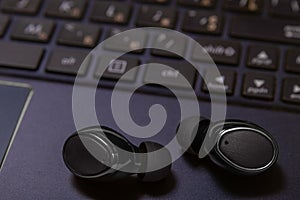 Close-up of wireless earpieces lying on a laptop keyboard