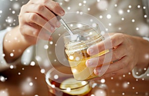 Close up of woman adding honey to tea with lemon