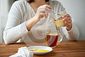 Close up of woman adding honey to tea with lemon