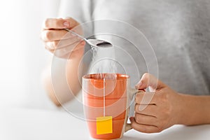 Close up of woman adding sugar to cup of tea