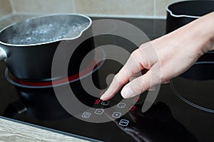 Close Up Of Woman Adjusting Temperature Of Halogen Hob In Kitchen