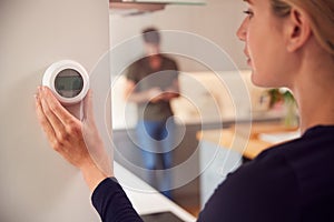 Close Up Of Woman Adjusting Wall Mounted Digital Central Heating Thermostat Control At Home