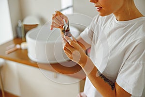 Close up of woman applying cosmetic serum onto her face in bathroom. Facial Skincare