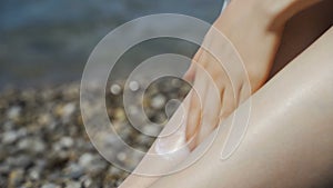 Close up of woman applying sunscreen to her legs on tropical beach