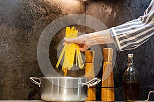 Close-up. A woman in an apron cooks spaghetti in the kitchen.
