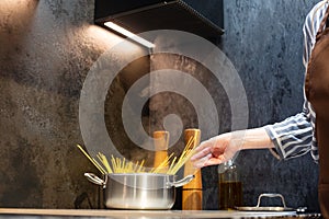 Close-up. A woman in an apron cooks spaghetti in the kitchen.