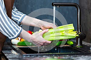 Close-up of a woman in an apron in the kitchen washing vegetables before preparing a vegetarian dish.