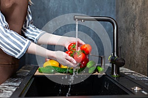 Close-up of a woman in an apron in the kitchen washing vegetables before preparing a vegetarian dish.