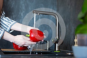 Close-up of a woman in an apron in the kitchen washing vegetables before preparing a vegetarian dish.