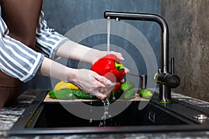 Close-up of a woman in an apron in the kitchen washing vegetables before preparing a vegetarian dish.