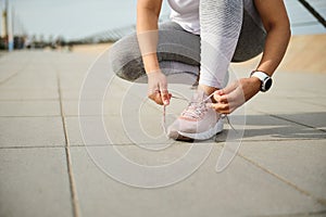 Close-up of a woman athlete runner jogger in gray leggings, tying laces on her pink sneakers, running shoes