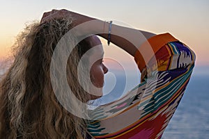 Close up of woman from back with hand in hair watching sunset and sea view from terrace of luxury holiday villa