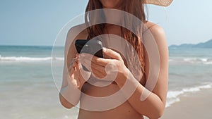 Close-up woman in bikini and hat on beach scrolling through social networks mobile phone. Female looks phone screen