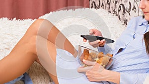 Close-up of a woman bored at home in front of the TV switches channels and eats junk food chicken wings.