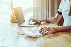 Close up of woman busy paying bills online on laptop calculating household finances or taxes at desk, using calculator