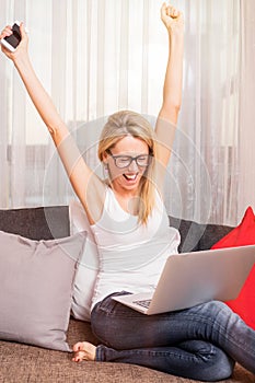 Close-up of woman celebrating her success with computer in her lap and cellphone in her hand