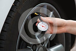 Close-Up Of Woman Checking Car Tyre Pressure With Gauge