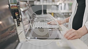 Close-up of a woman choosing a laptop in an electronics hypermarket, with only her hands in the frame