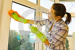 Close-up of woman cleaning windows, hands in rubber protective gloves, rag and sprayer detergent