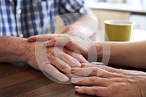 Close Up Of Woman Comforting Unhappy Senior Man Sitting In Kitchen At Home