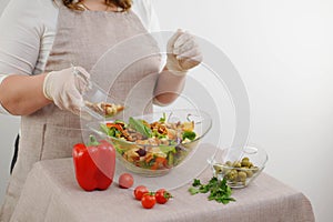 close-up woman cook in gloves pours nuts into salad ingredients on table apron for kitchen pepper tomatoes parsley