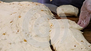 Close up for woman in cooking gloves cutting the dough into pieces with a special knife. Stock footage. Women hands cut