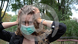 Close-up woman in coronavirus face mask holding head in hands having panic attack outdoors looking at camera. Portrait