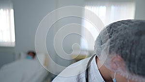 Close-up woman in coronavirus uniform looking at camera leaving hospital ward with ill patients at background. Young